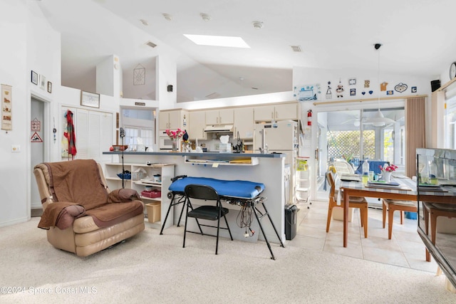 kitchen with cream cabinetry, hanging light fixtures, light colored carpet, and high vaulted ceiling