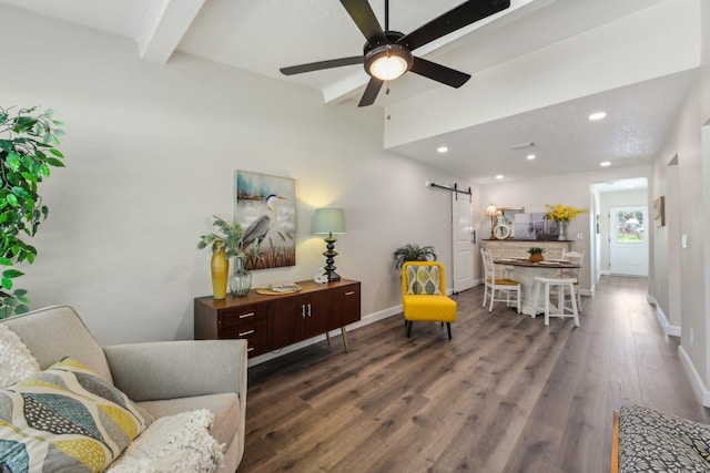 living area featuring beam ceiling, a barn door, dark wood-type flooring, and ceiling fan