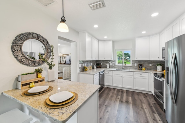 kitchen with sink, white cabinets, decorative light fixtures, appliances with stainless steel finishes, and dark hardwood / wood-style flooring