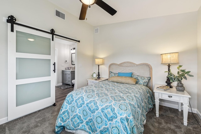 bedroom featuring dark carpet, connected bathroom, a barn door, and ceiling fan