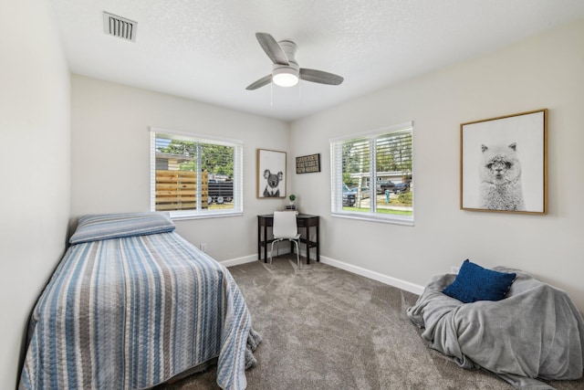 bedroom featuring ceiling fan, a textured ceiling, multiple windows, and carpet floors