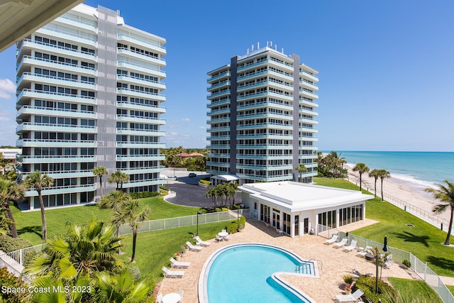 view of swimming pool with a water view, a patio area, a yard, and a beach view