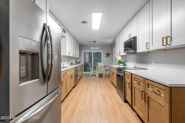 kitchen featuring light stone countertops, white cabinets, stainless steel appliances, and light wood-type flooring