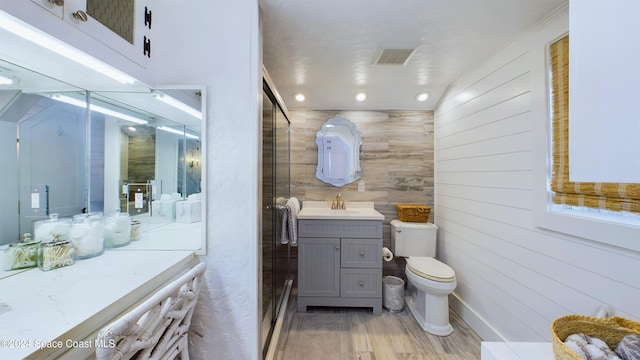 bathroom featuring hardwood / wood-style floors, vanity, wooden walls, and toilet