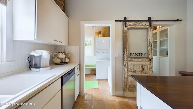 kitchen featuring a barn door, stainless steel dishwasher, white cabinets, and stacked washer / drying machine