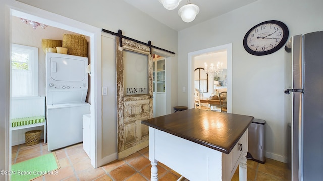 interior space featuring an inviting chandelier, a barn door, a kitchen island, stacked washer and dryer, and stainless steel fridge