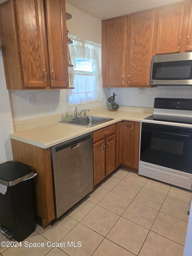 kitchen with appliances with stainless steel finishes, decorative backsplash, sink, and light tile patterned floors