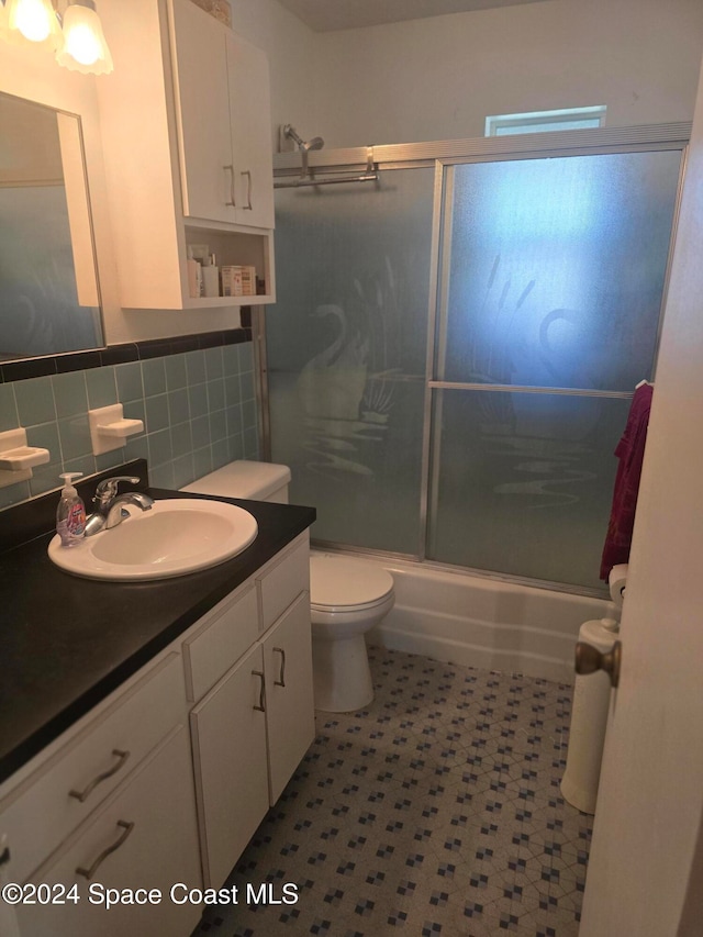 full bathroom featuring vanity, bath / shower combo with glass door, toilet, and tasteful backsplash