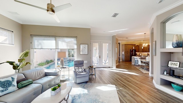 living room featuring plenty of natural light, ornamental molding, ceiling fan with notable chandelier, and hardwood / wood-style flooring