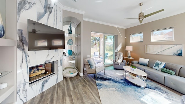 living room featuring hardwood / wood-style flooring, ceiling fan, crown molding, and a high end fireplace