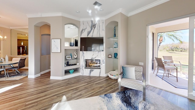 sitting room featuring a high end fireplace, an inviting chandelier, built in shelves, ornamental molding, and wood-type flooring