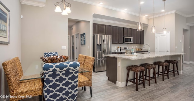 kitchen with a kitchen island with sink, stainless steel appliances, a breakfast bar, decorative light fixtures, and light hardwood / wood-style floors