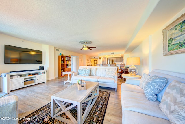 living room with a textured ceiling, light wood-type flooring, and ceiling fan