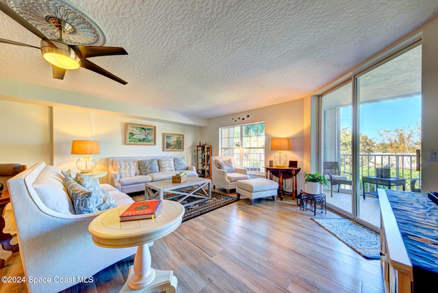 living room featuring ceiling fan, a textured ceiling, light hardwood / wood-style flooring, and a wall of windows