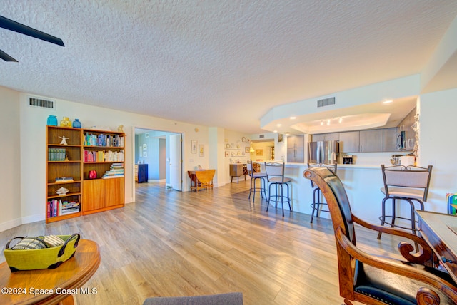 living room with a textured ceiling, light wood-type flooring, and ceiling fan