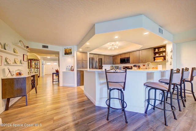 kitchen with light hardwood / wood-style flooring, appliances with stainless steel finishes, a textured ceiling, kitchen peninsula, and a breakfast bar