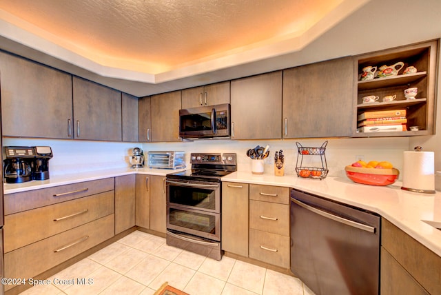 kitchen with a textured ceiling, stainless steel appliances, a tray ceiling, and light tile patterned floors