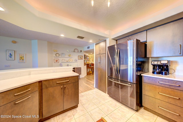 kitchen with a textured ceiling, light tile patterned floors, and stainless steel refrigerator