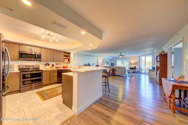 kitchen with ceiling fan, a breakfast bar, a textured ceiling, light hardwood / wood-style floors, and stainless steel appliances