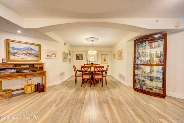 dining room with vaulted ceiling, a textured ceiling, and light hardwood / wood-style floors