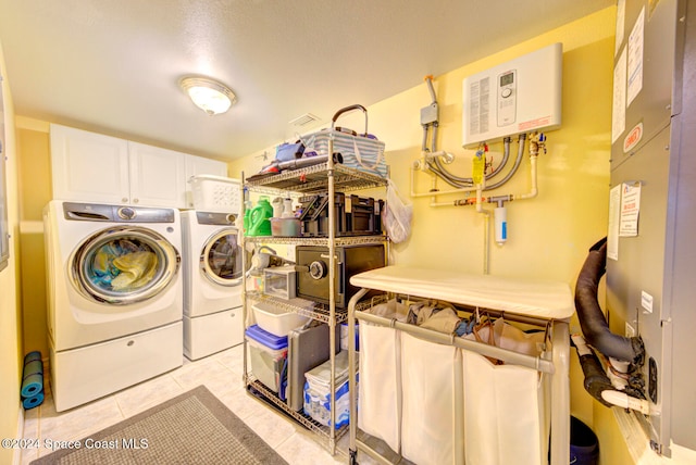 clothes washing area featuring cabinets, water heater, washer and clothes dryer, and light tile patterned floors