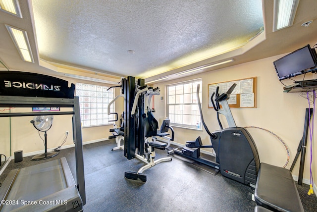 workout room featuring a textured ceiling, a healthy amount of sunlight, and a tray ceiling