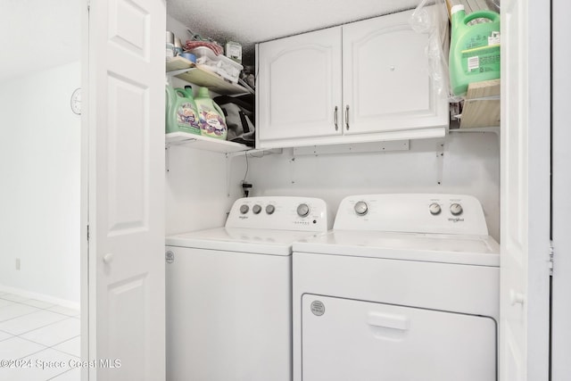 laundry area with cabinets, a textured ceiling, washer and clothes dryer, and light tile patterned floors