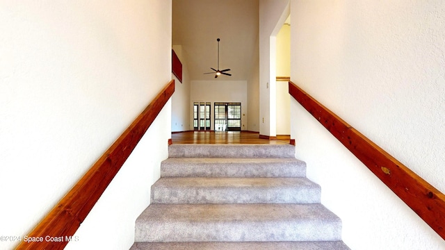 stairs with hardwood / wood-style floors, ceiling fan, and a high ceiling