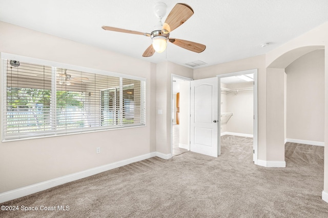 unfurnished bedroom featuring light carpet, a walk in closet, a closet, and ceiling fan