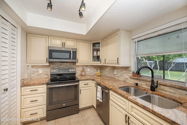 kitchen featuring light stone counters, cream cabinets, stainless steel appliances, and sink