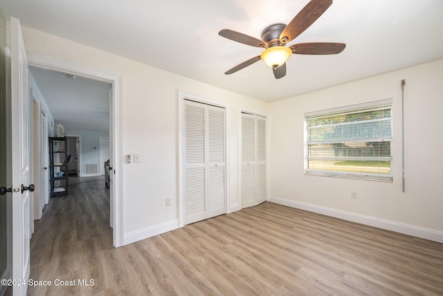 unfurnished bedroom with multiple closets, ceiling fan, and light wood-type flooring