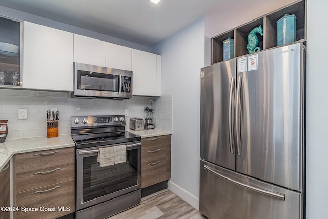 kitchen featuring light stone counters, appliances with stainless steel finishes, light hardwood / wood-style flooring, and white cabinetry