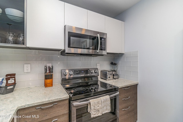 kitchen with white cabinetry, light stone counters, stainless steel appliances, and backsplash