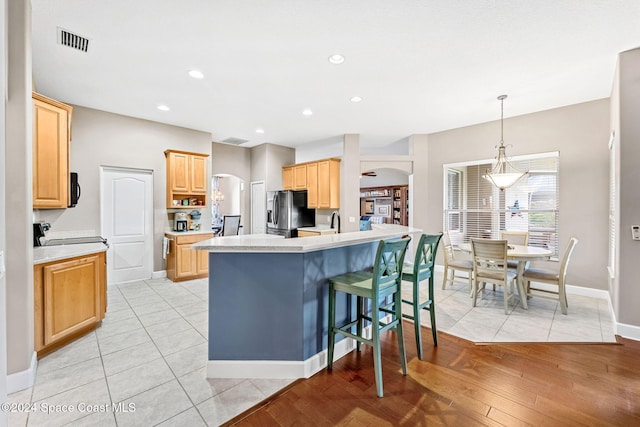 kitchen featuring light brown cabinets, stainless steel refrigerator with ice dispenser, light hardwood / wood-style flooring, and a center island with sink