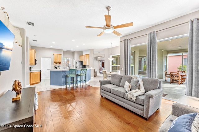 living room with ceiling fan, a textured ceiling, and light hardwood / wood-style flooring