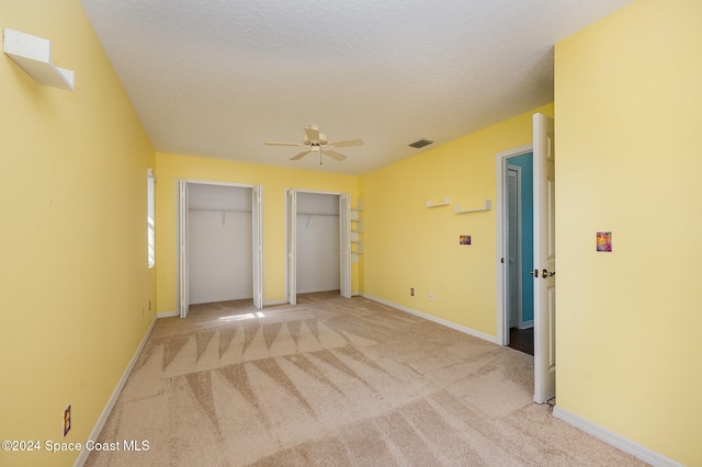 unfurnished bedroom with ceiling fan, two closets, light colored carpet, and a textured ceiling