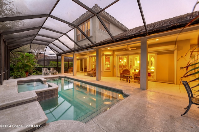 pool at dusk featuring an in ground hot tub, glass enclosure, ceiling fan, and a patio area