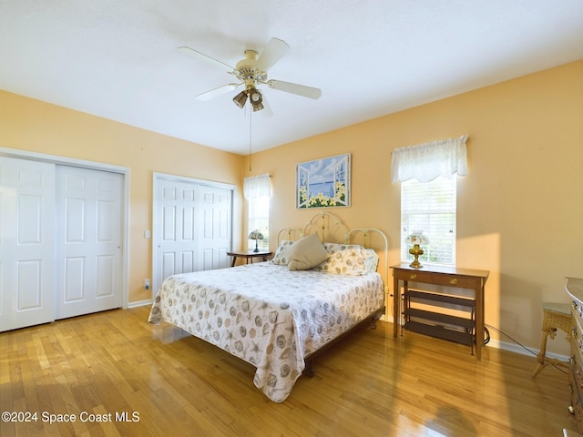 bedroom with light hardwood / wood-style flooring, two closets, and ceiling fan