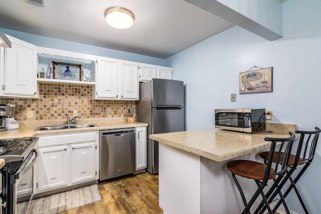 kitchen with kitchen peninsula, appliances with stainless steel finishes, a kitchen breakfast bar, dark hardwood / wood-style floors, and white cabinets