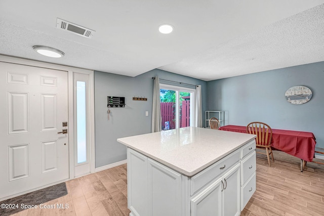 kitchen featuring a center island, white cabinets, a textured ceiling, and light wood-type flooring