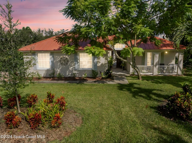 view of front of house featuring a yard, covered porch, metal roof, and stucco siding