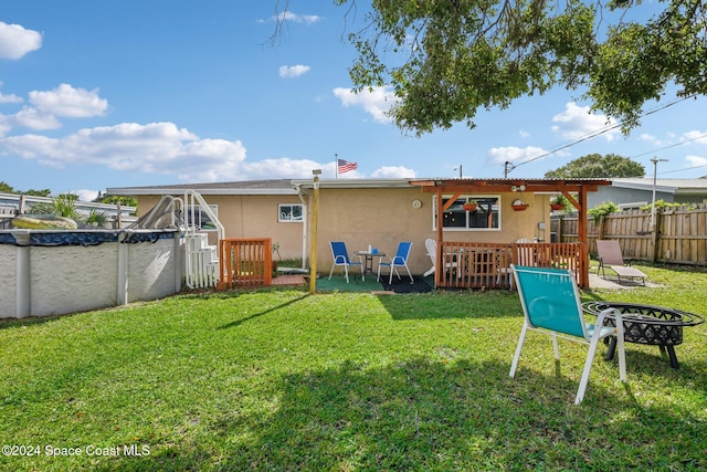 rear view of property featuring a patio area, a covered pool, and a lawn