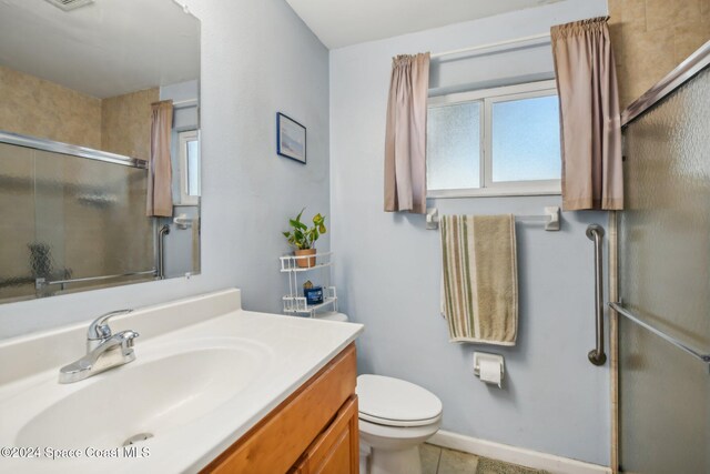 bathroom with a shower with door, vanity, toilet, and tile patterned flooring