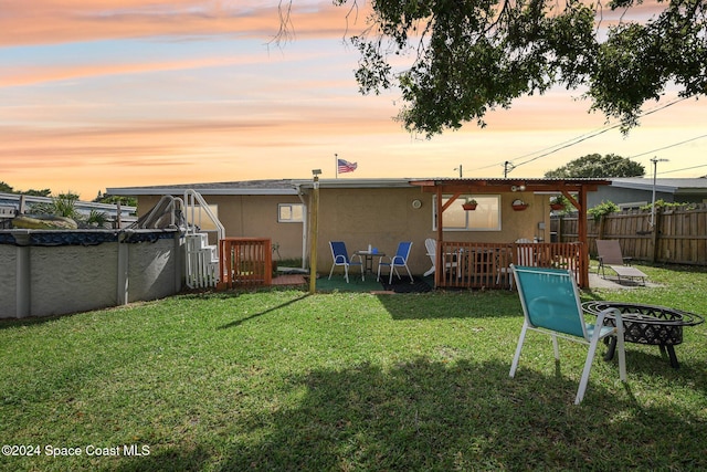 back house at dusk featuring a patio, a covered pool, and a lawn