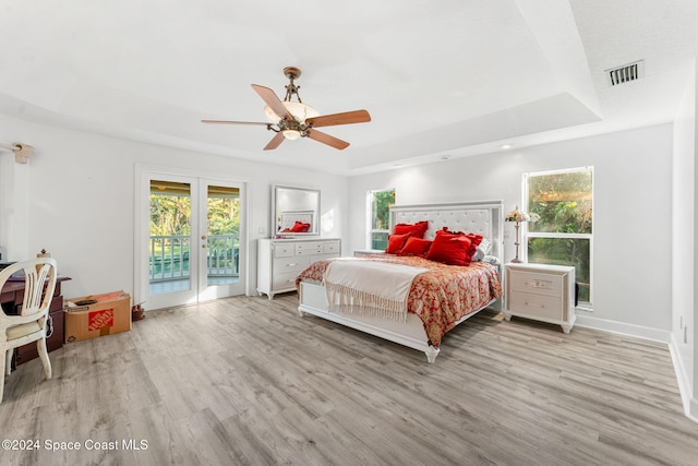 bedroom with access to outside, light wood-type flooring, french doors, a raised ceiling, and ceiling fan