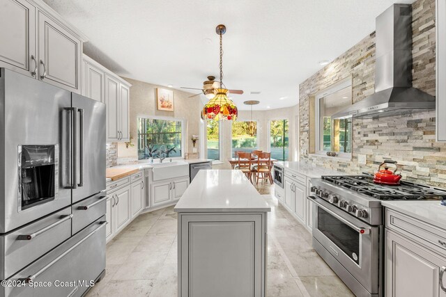 kitchen with a wealth of natural light, a center island, appliances with stainless steel finishes, and wall chimney range hood