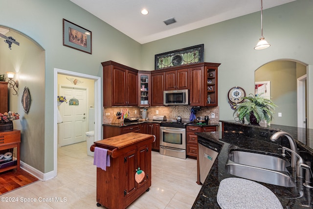 kitchen featuring decorative backsplash, hanging light fixtures, stainless steel appliances, dark stone countertops, and sink