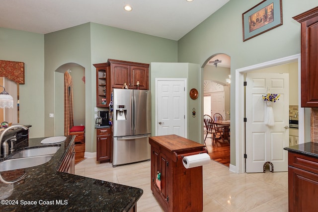 kitchen with a kitchen island, stainless steel fridge with ice dispenser, high vaulted ceiling, dark stone countertops, and sink