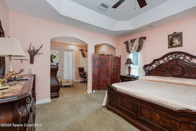 bedroom featuring light carpet, a tray ceiling, and ceiling fan