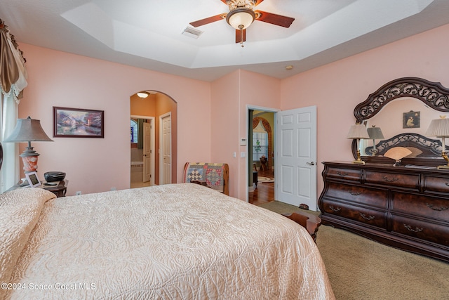 carpeted bedroom with ceiling fan, a tray ceiling, and ensuite bath